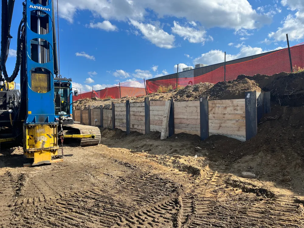 A construction site featuring a large drilling machine next to a dirt mound and reinforced wooden walls.