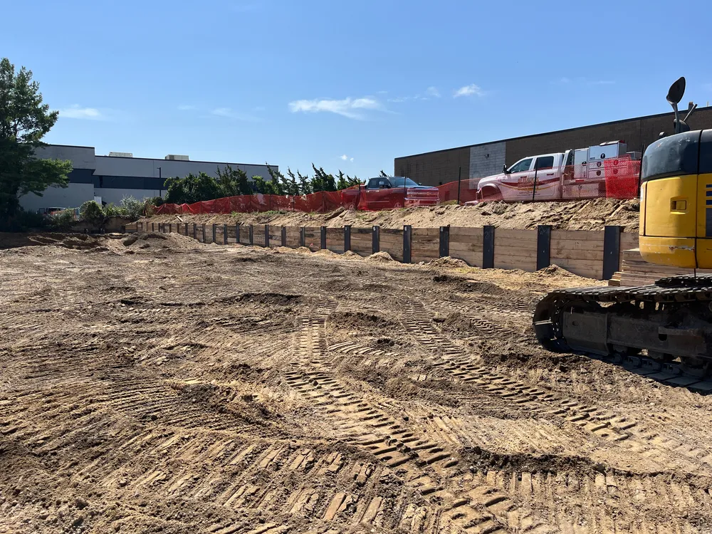 Construction site with a cleared area, heavy machinery, and a barrier of orange fencing.