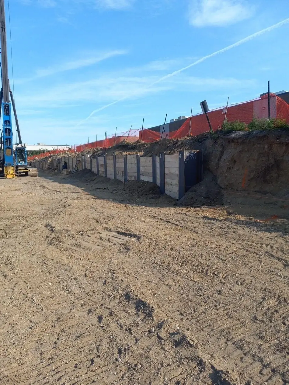 A construction site with a trench lined by what appears to be concrete forms or panels, surrounded by dirt and machinery.