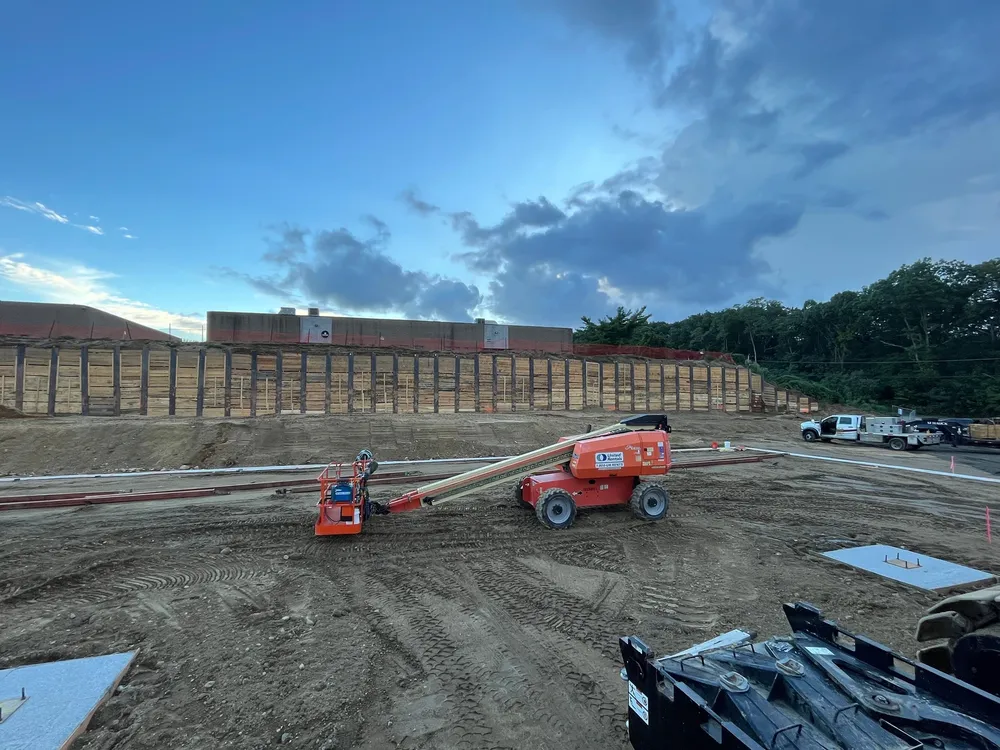 Construction site with heavy machinery and a large wooden structure being built, under a cloudy sky.