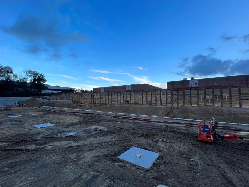 Construction site with a partially built structure, dirt, and machinery under a blue sky.