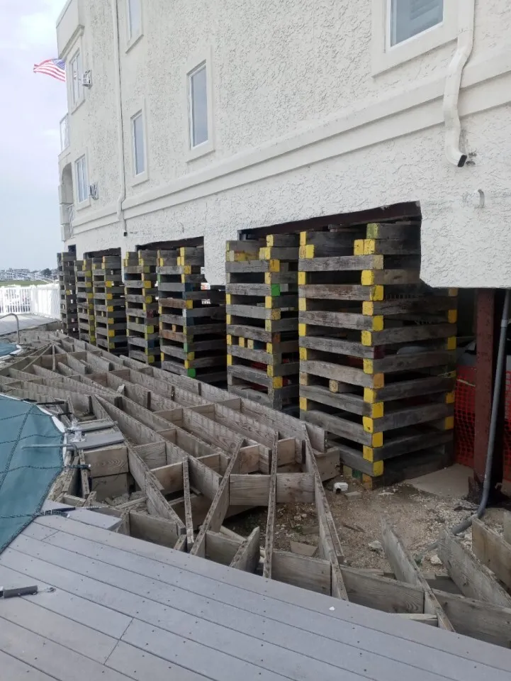 A building foundation supported by wooden pallets and braces, with a partially excavated area.