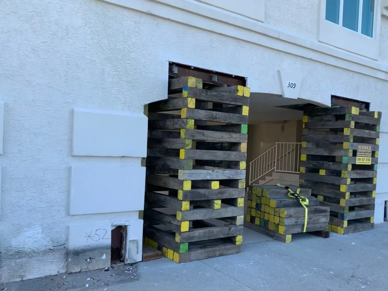 A building entrance supported by large wooden pallets stacked on either side.