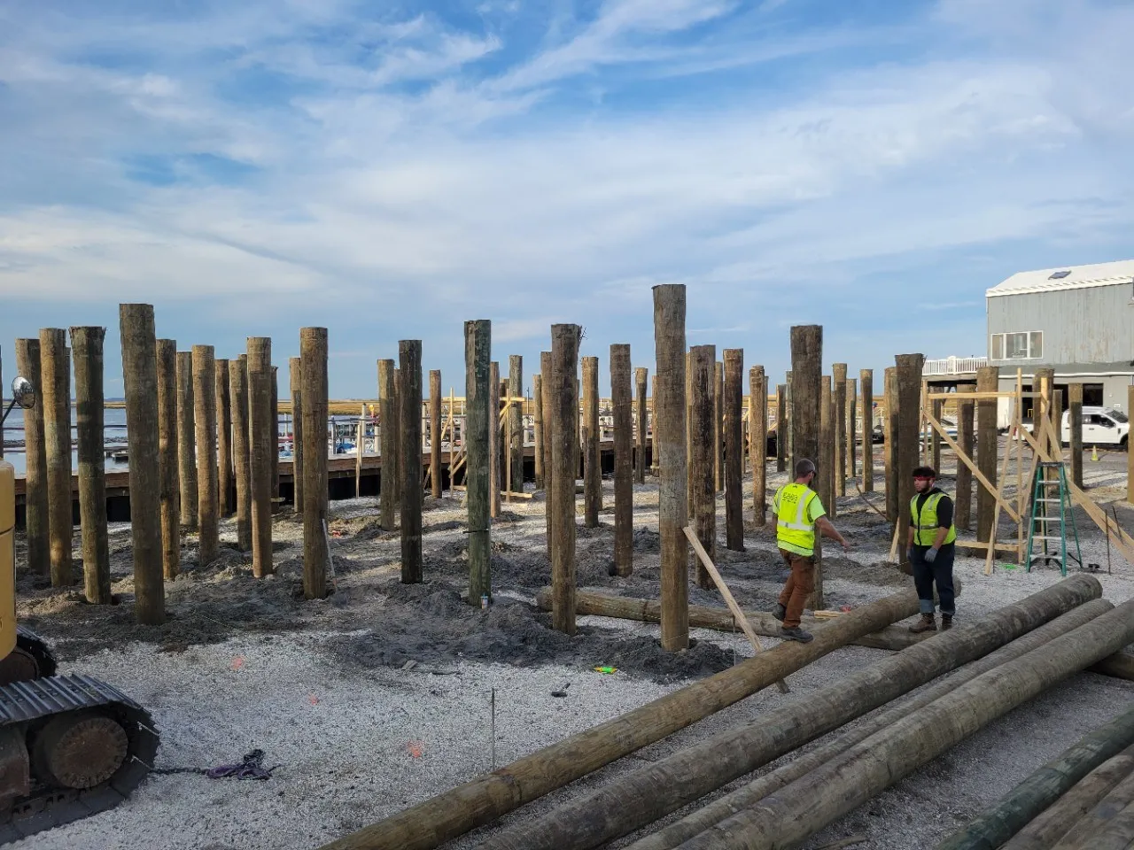Construction site with wooden piles and workers in safety vests.