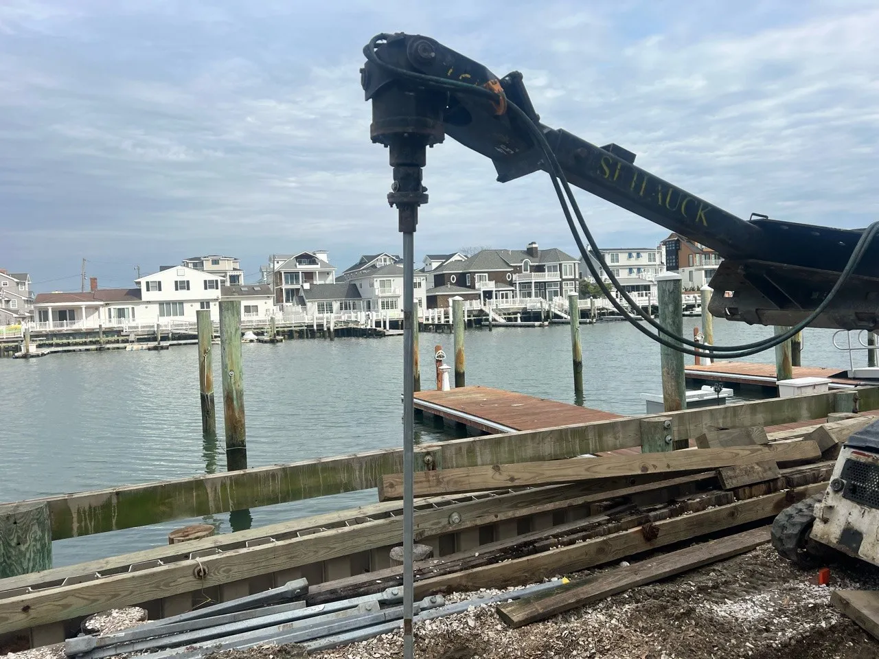 A construction site by the water featuring machinery and a view of residential buildings across the water.