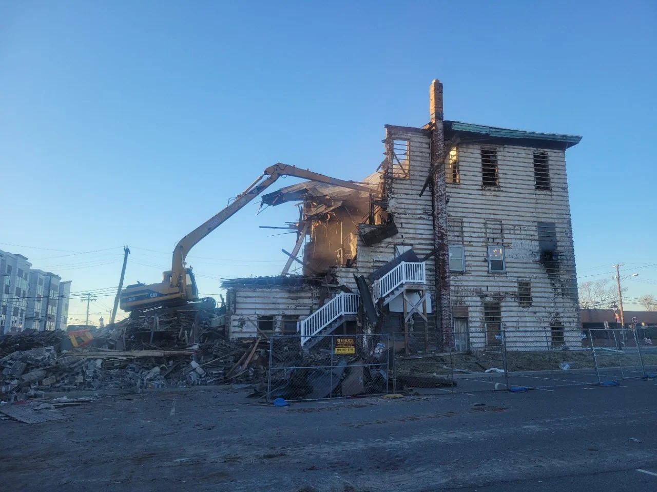 Construction machinery demolishing a partially collapsed building on a clear day.