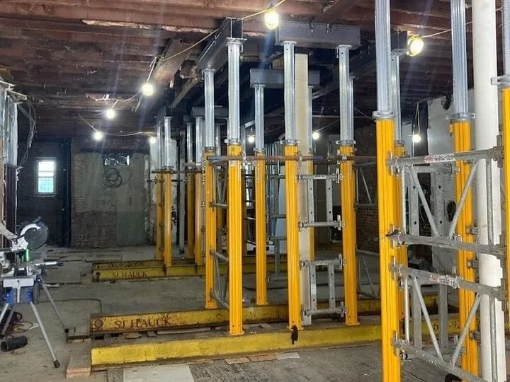 A construction site with several vertical supports set up in a dimly lit space, featuring scaffolding and other construction equipment.