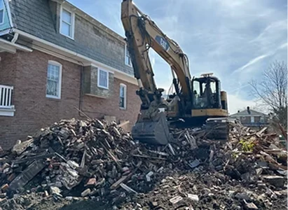 A large excavator working on a pile of debris and bricks near a building.