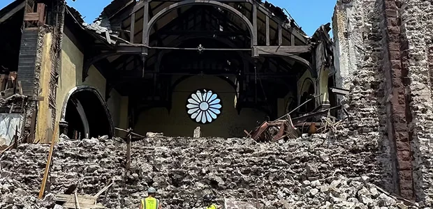 A ruined interior of a church with a collapsed ceiling and a large stained glass window in the background.