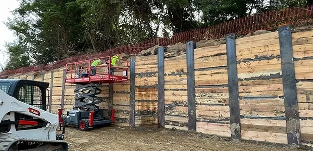 A construction site showing workers on a scissor lift alongside a wooden retaining wall.