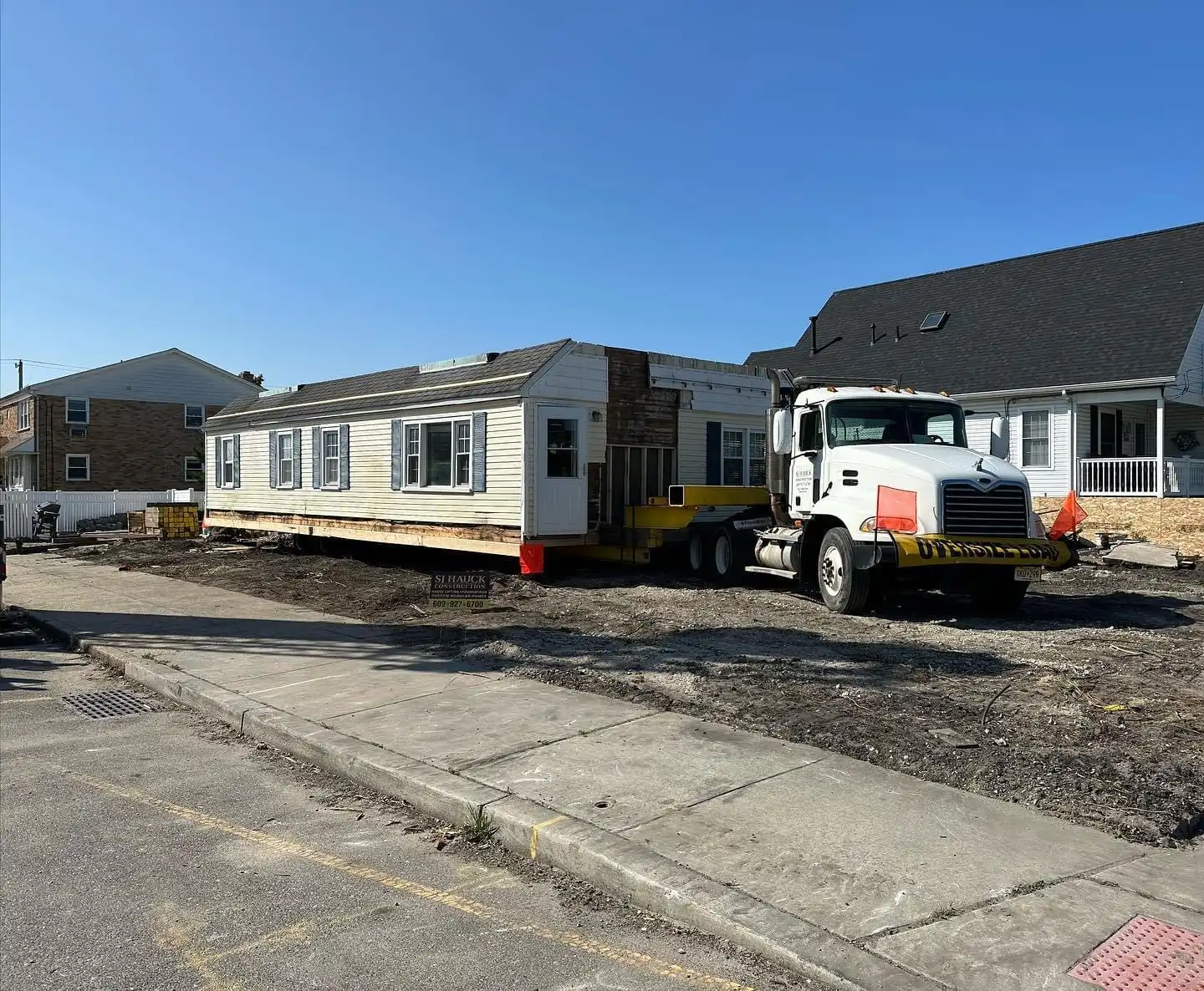 A mobile home being transported on a trailer in an empty lot.