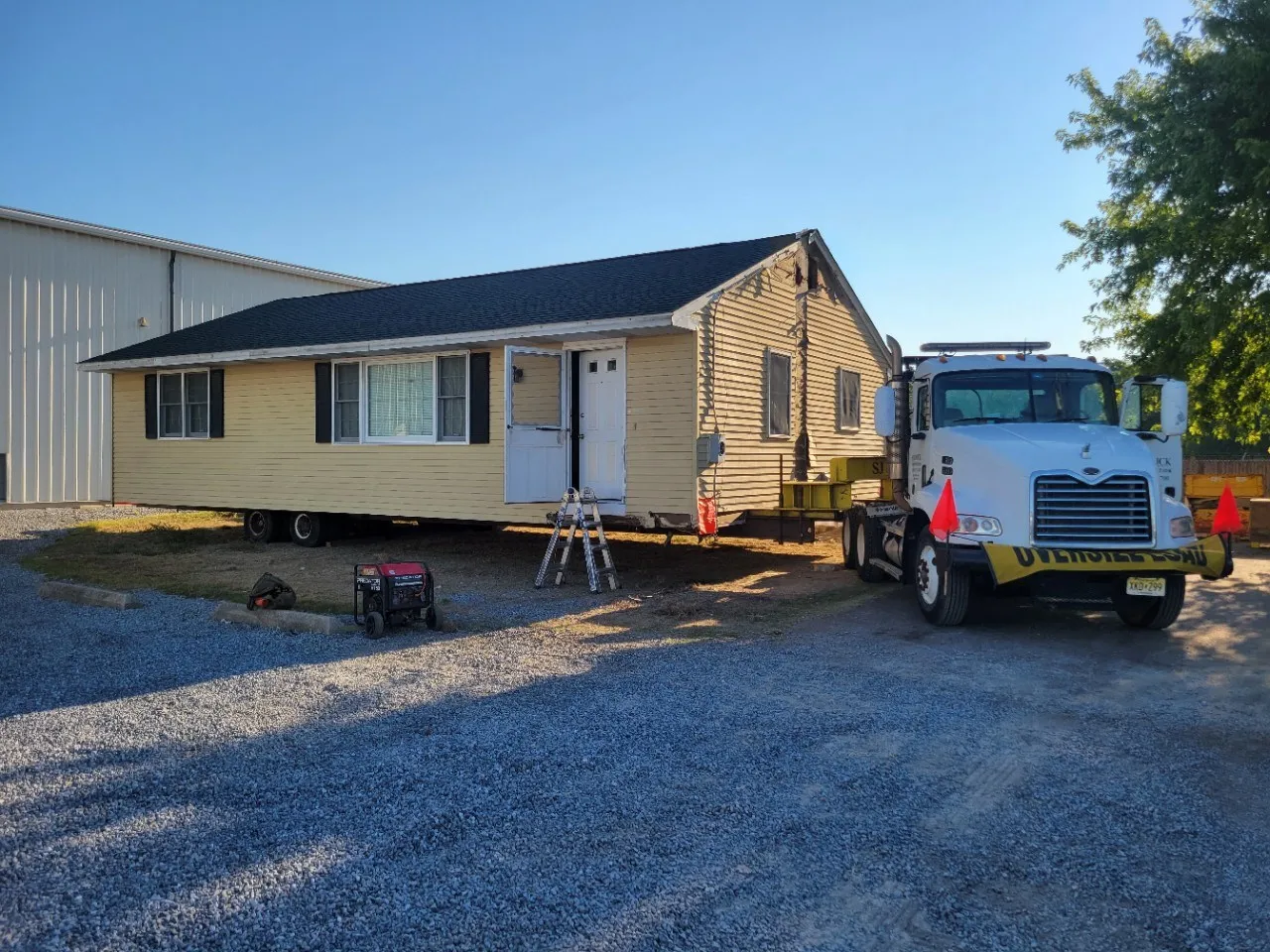 A mobile home next to a truck, positioned on a gravel lot with construction tools and equipment nearby.
