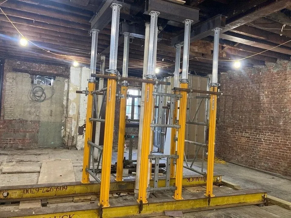 Construction site with metal scaffolding and supports in a room with exposed brick walls and wooden beams.