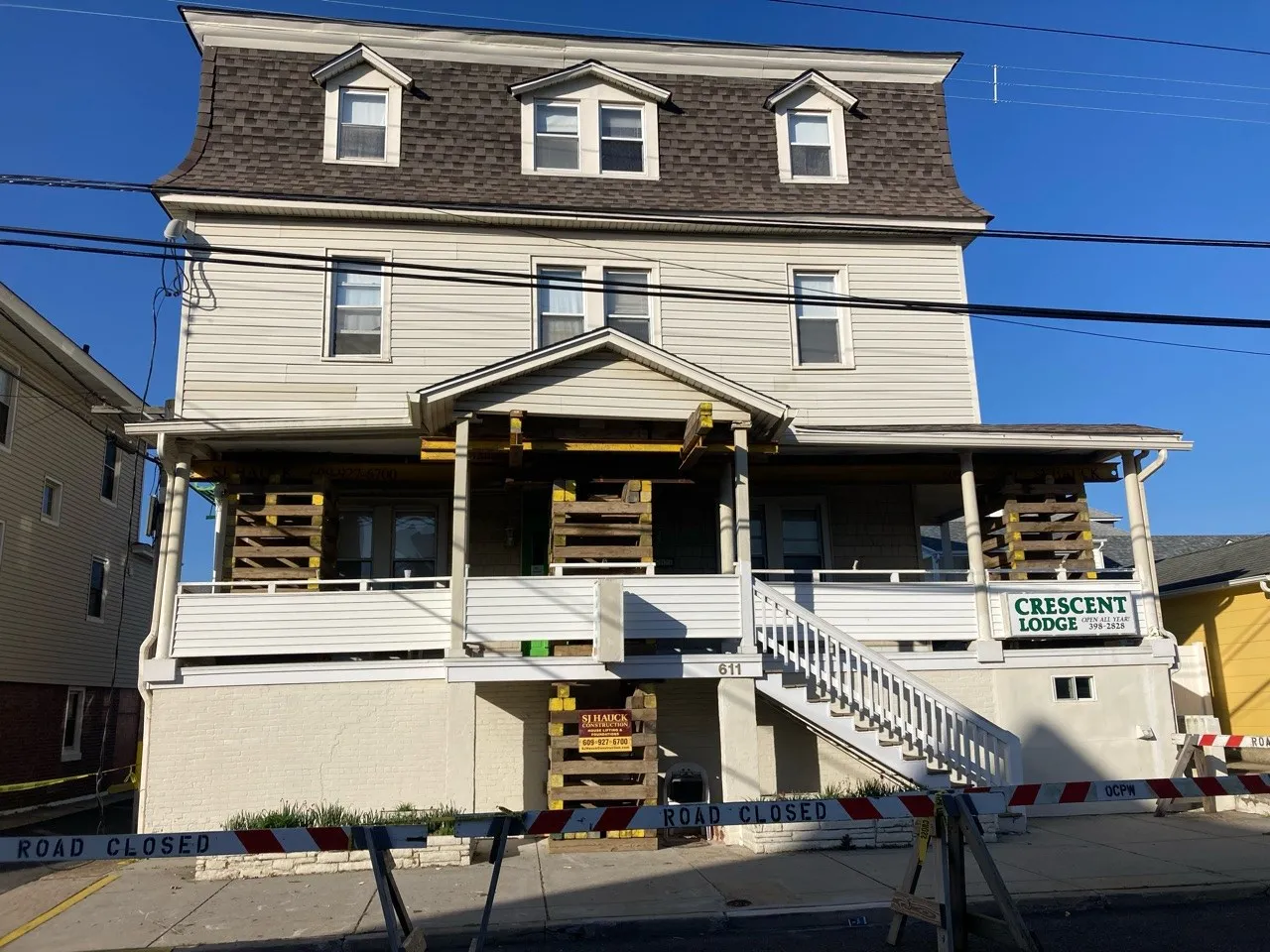A three-story house with a sign reading "Crescent Lodge," featuring wooden supports on the porch and a road closed barrier in front.