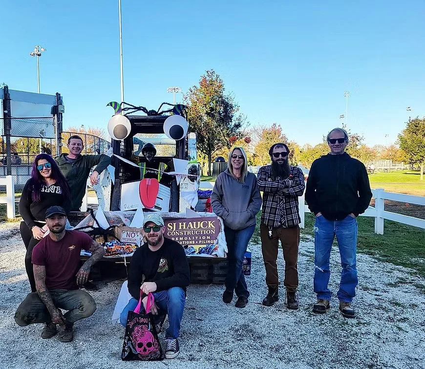 A group of people posing in front of a decorated vehicle, featuring various props and decorations, outdoors in a park-like setting.