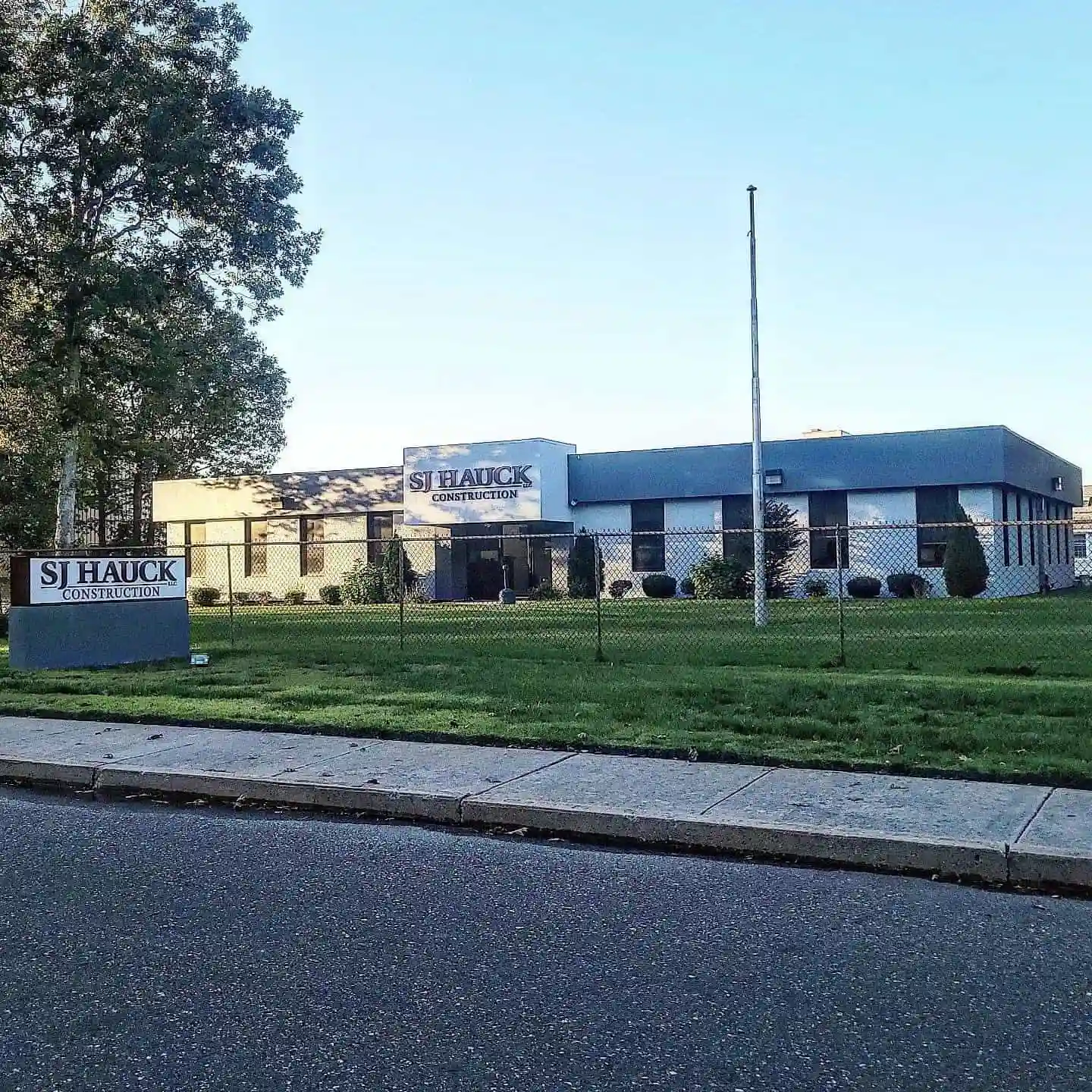 A building with the sign "SJ Hauck Construction" in front, surrounded by a lawn and a fence.