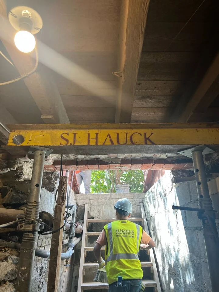Exterior view of the historic three-story Ventnor Square Theatre building undergoing structural renovation, supported by wooden shoring beams and cribbing stacks behind a chain-link construction fence.