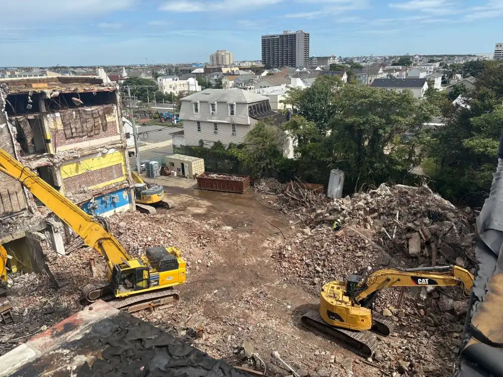 Aerial high-angle view of an active demolition site showing heavy yellow excavators surrounded by piles of rubble near a partially demolished brick building.